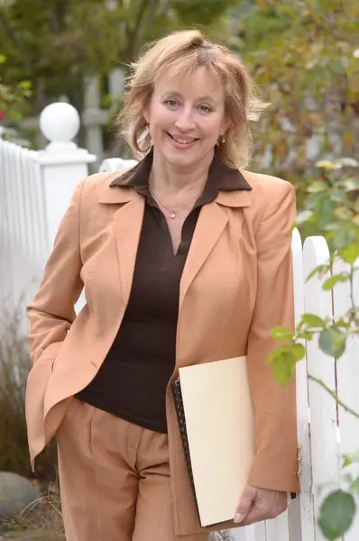Laurie Pfohl, East Bay real estate agent, standing next to a white picket fence and smiling.