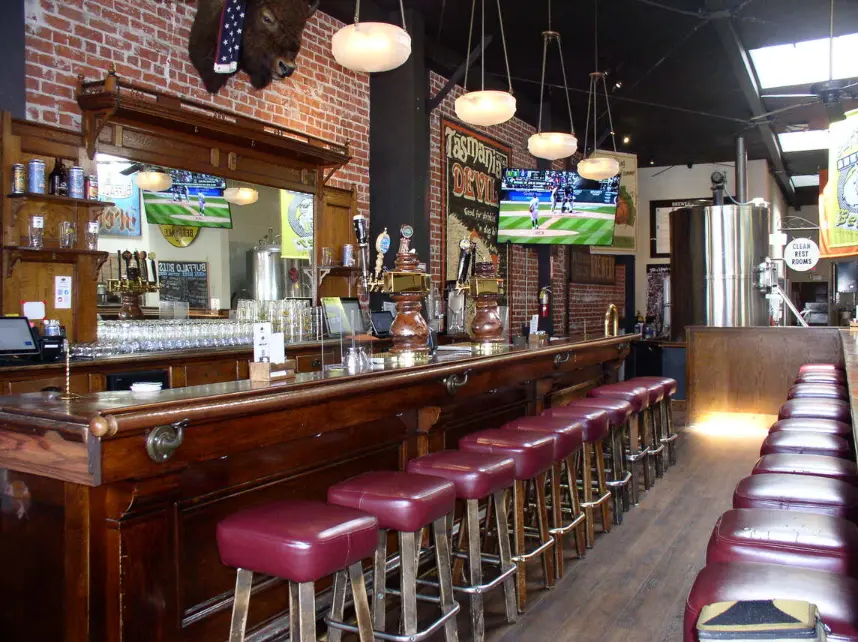 Photo of the bar at Buffalo Bill's Brewery in Hayward, CA, showcasing the bar counter, seating area, and various drink options.